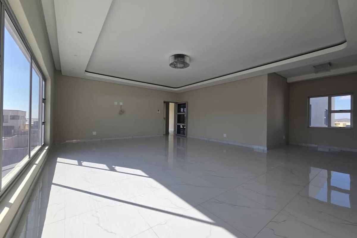 A spacious, sunlit living area featuring modern marble-look floor tiles, a sophisticated recessed ceiling design, and large windows providing ample natural light.