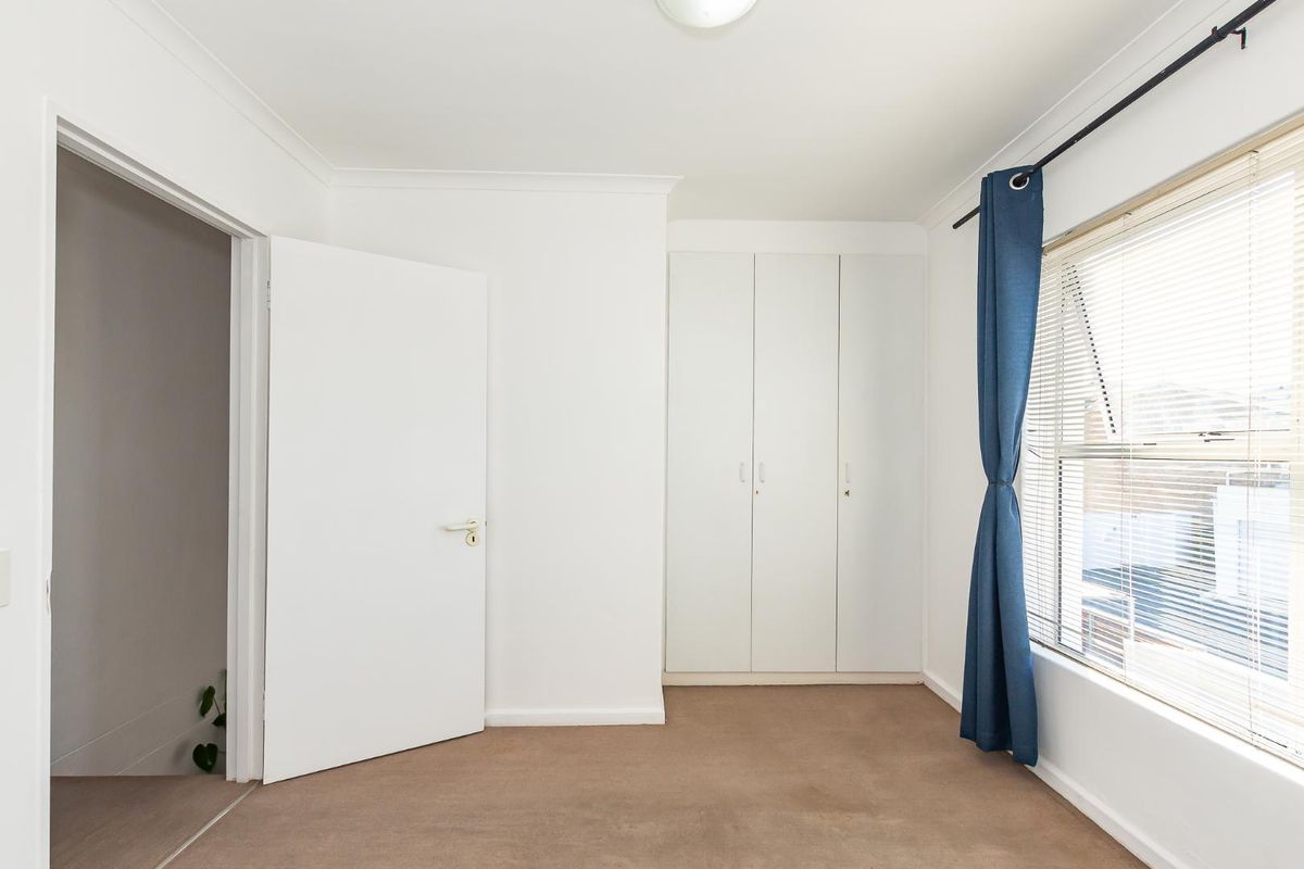 A bright bedroom featuring neutral carpeting, built-in wardrobes, and a window with fitted blinds.