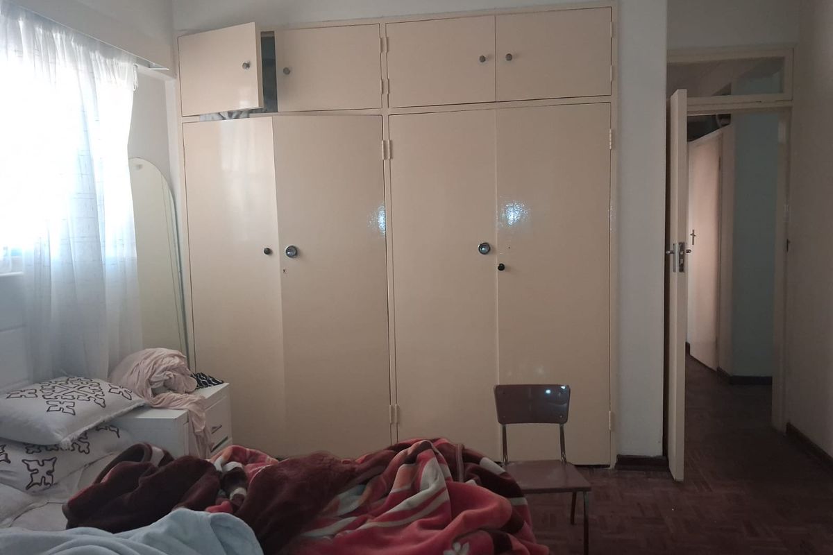 Bedroom featuring built-in cupboards and parquet flooring. The space requires cosmetic updates to improve the overall aesthetic and functionality.