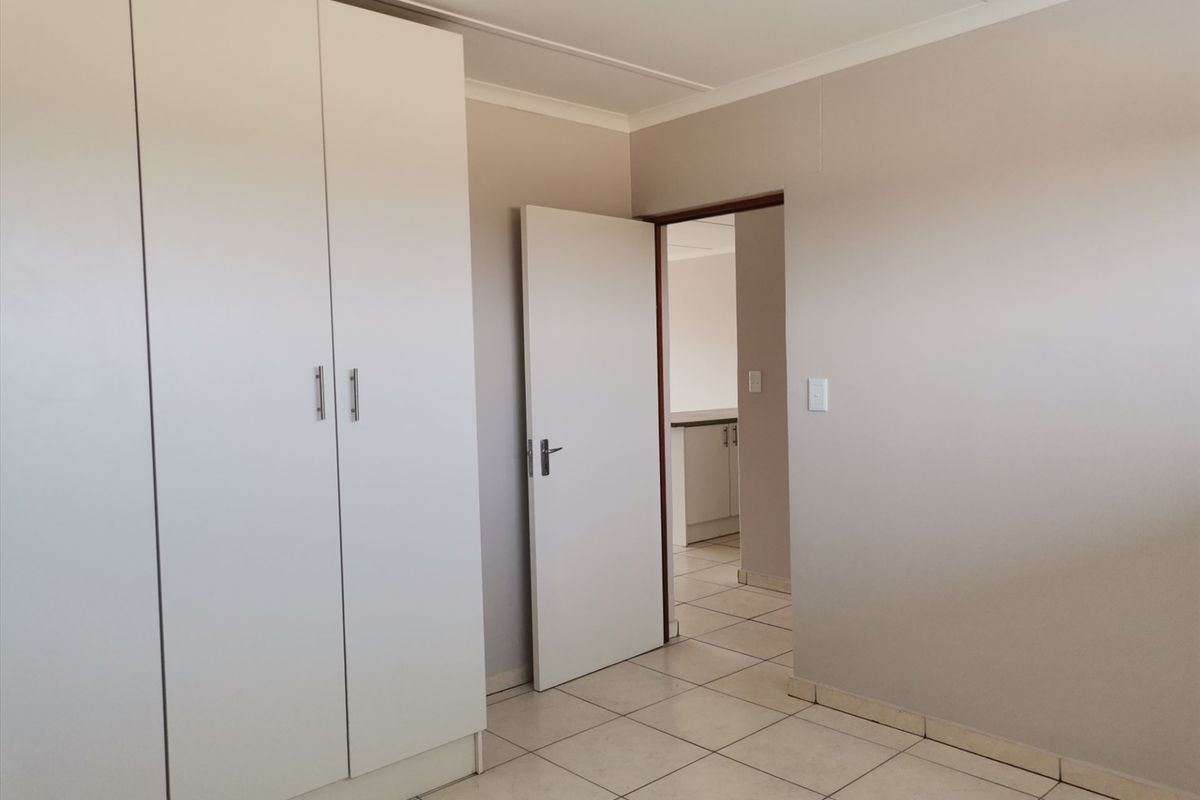 A clean, empty bedroom featuring neutral wall tones, tiled flooring, and built-in cupboards, offering a versatile space ready for personalization.