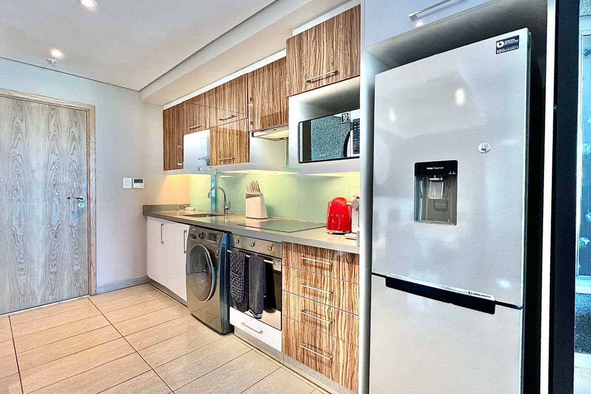 Modern kitchen featuring wood-grain cabinetry, integrated oven, hob, extractor fan, and built-in microwave, complemented by sleek tiled flooring and contemporary finishes.