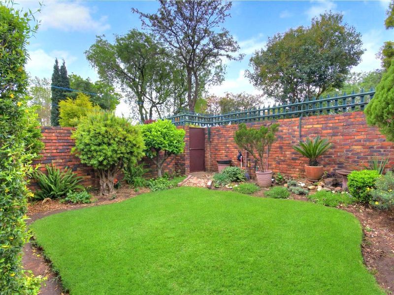 A private, well-maintained rear garden featuring a lush green lawn, established perimeter landscaping, and a secure brick boundary wall with a pedestrian gate.