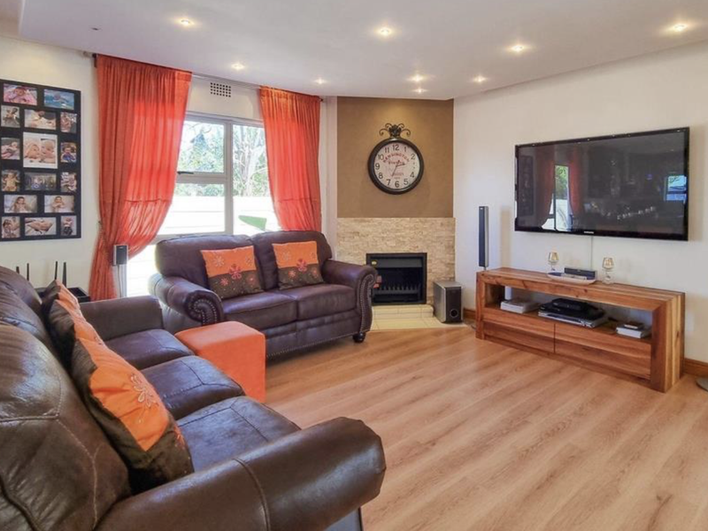 A comfortable living room featuring laminate flooring, recessed downlighting, and a built-in fireplace with a decorative stone-clad surround.