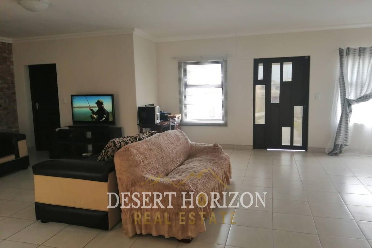 Spacious living room featuring neutral tiled flooring, a modern front door, and natural light through window blinds.