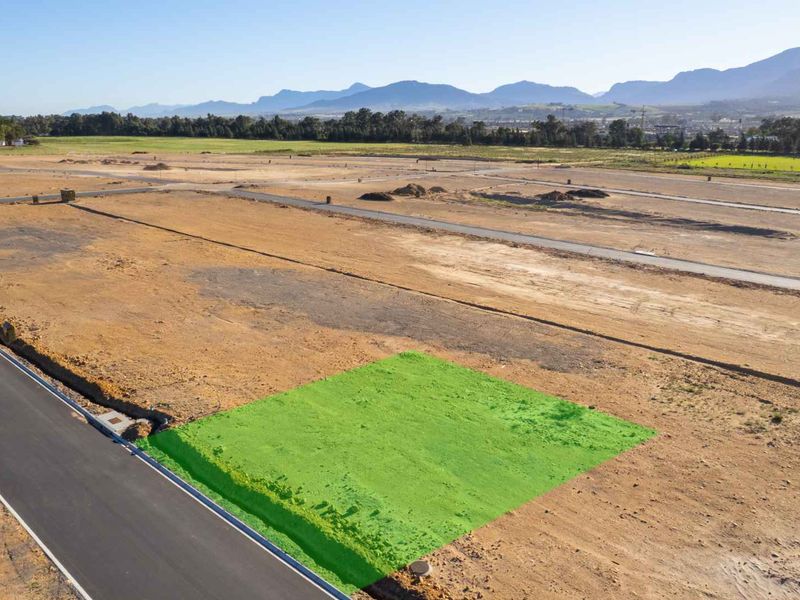 Aerial view of a vacant residential plot in a developing estate, featuring road access and mountain views.