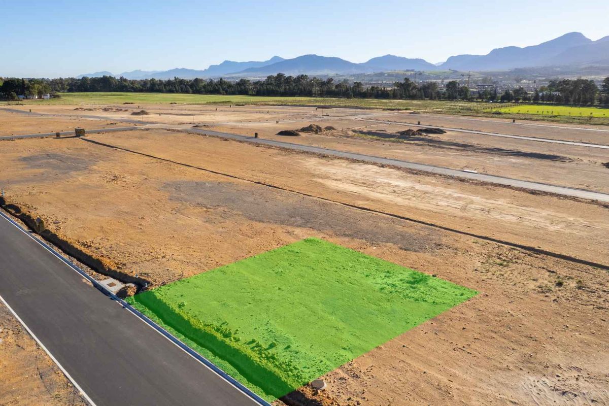 Aerial view of a vacant residential plot in a developing estate, featuring road access and mountain views.