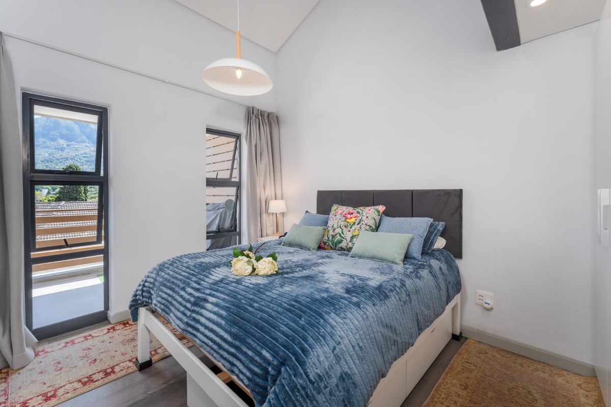 A bright bedroom featuring a vaulted ceiling, modern aluminium window frames, and a built-in wardrobe with access to an outdoor balcony area.