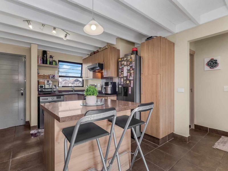 A functional kitchen featuring wood-finish cabinetry, a stone-topped island, exposed beam ceilings, and tiled flooring, offering a practical and well-lit cooking space.