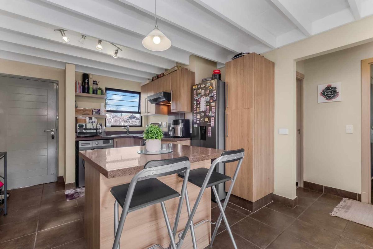 A functional kitchen featuring wood-finish cabinetry, a stone-topped island, exposed beam ceilings, and tiled flooring, offering a practical and well-lit cooking space.