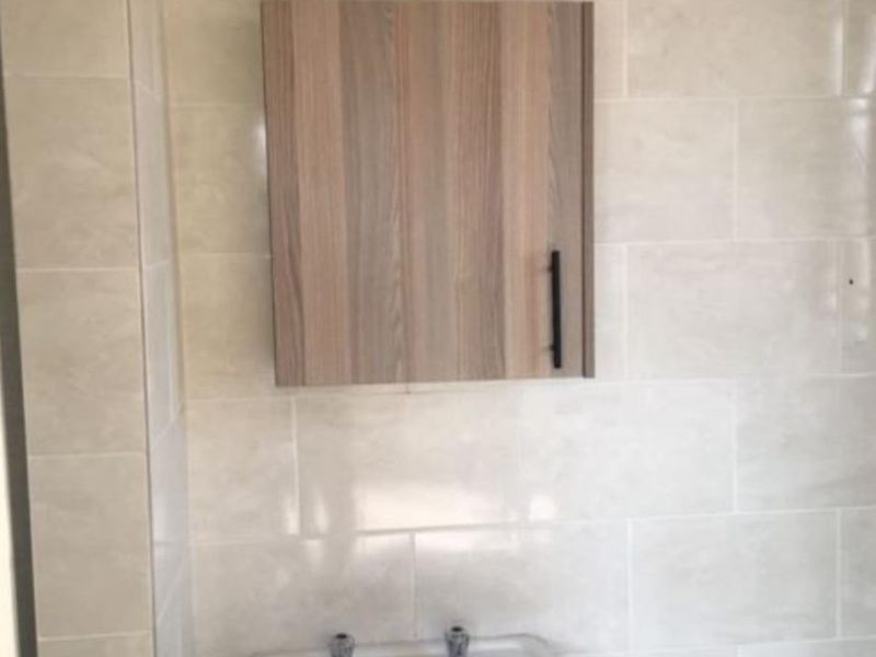 A simple bathroom area featuring a pedestal basin and a wall-mounted wooden medicine cabinet against neutral tiled walls.