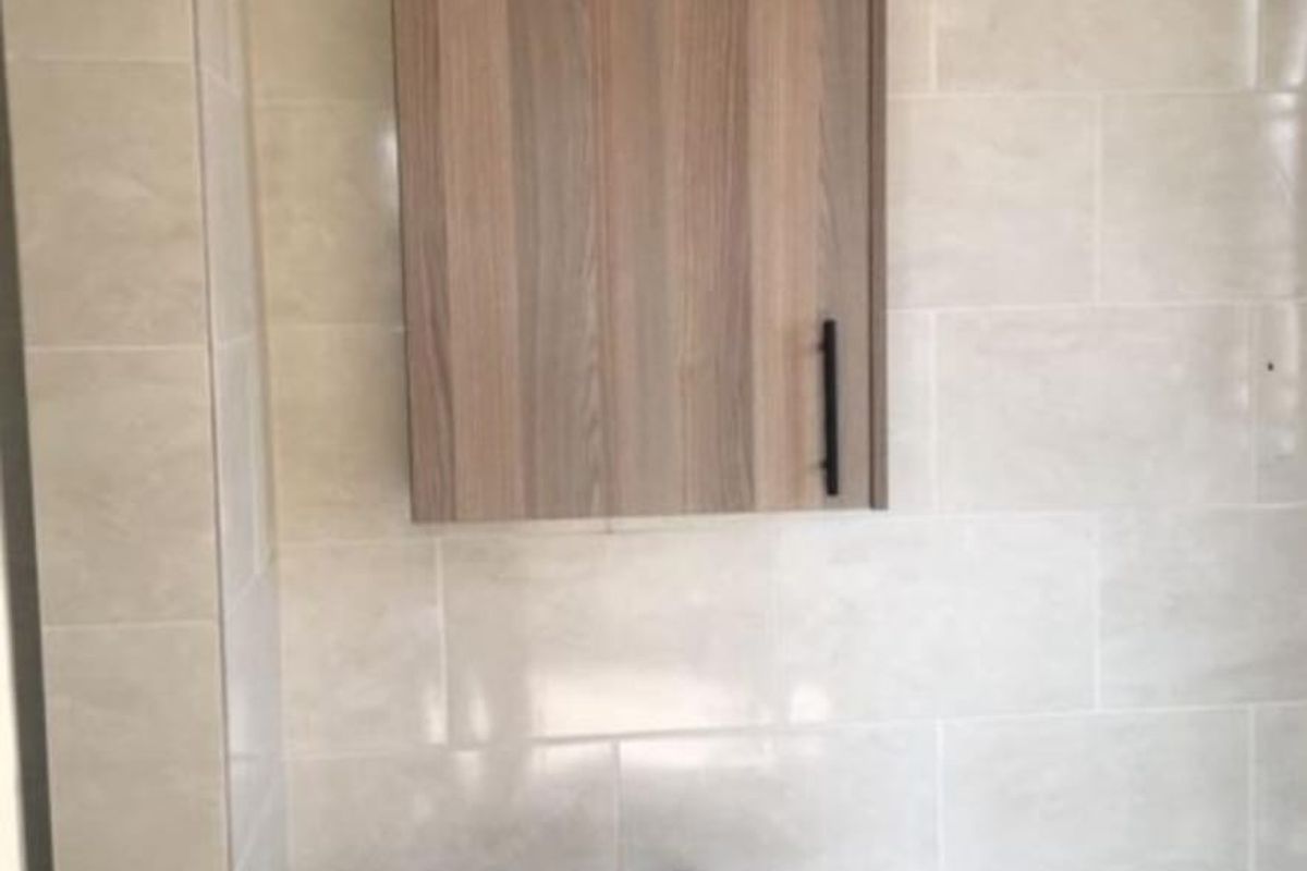 A simple bathroom area featuring a pedestal basin and a wall-mounted wooden medicine cabinet against neutral tiled walls.