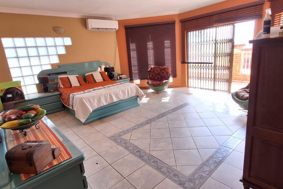 Spacious bedroom featuring tiled flooring, a split-system air conditioner, and large glass block windows with access to an outdoor area via a security gate.