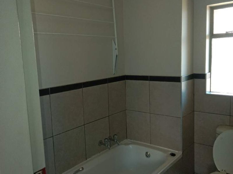 A functional bathroom featuring a bathtub, toilet, and wall-mounted drying rack with neutral wall tiles and wood-look floor tiles.