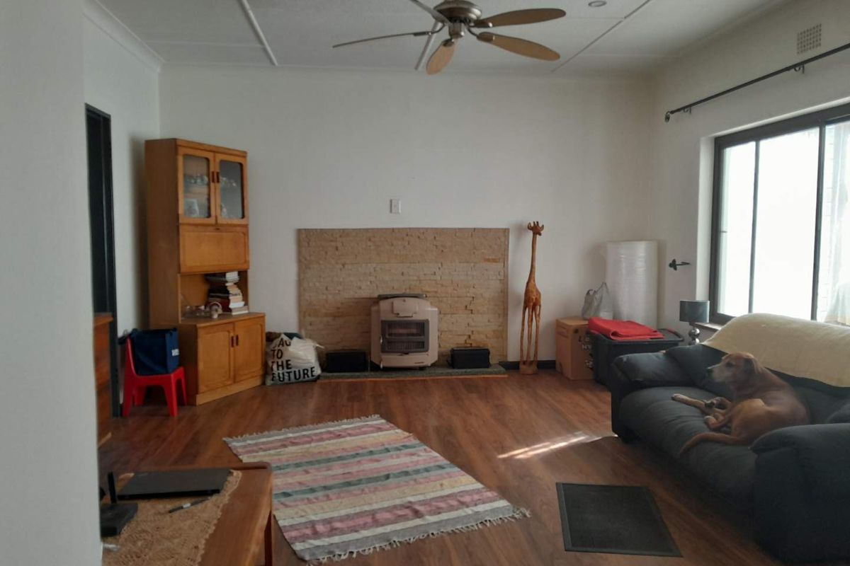 Spacious living room featuring wood-look laminate flooring, a stone fireplace surround, and a ceiling fan, offering a comfortable and functional layout.