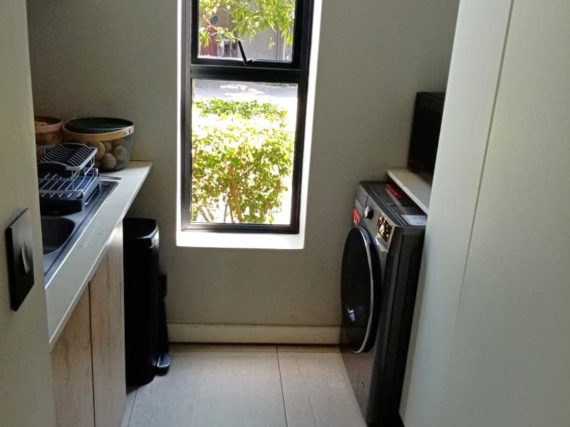 A compact, modern laundry room featuring built-in cabinetry, a sink, and tiled flooring, with a vertical window providing natural light.