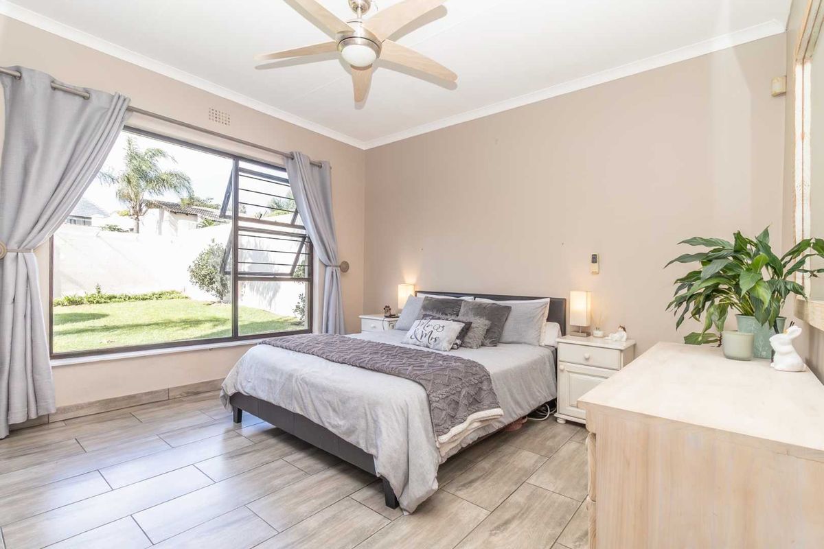 A well-lit bedroom featuring large windows with garden views, tiled flooring, and a ceiling fan.