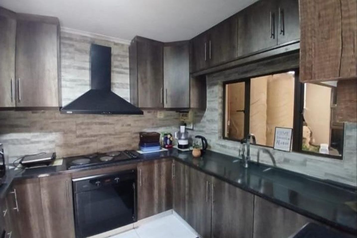 Modern kitchen featuring dark wood cabinetry, black stone countertops, built-in oven, electric hob, and a stylish tiled backsplash.