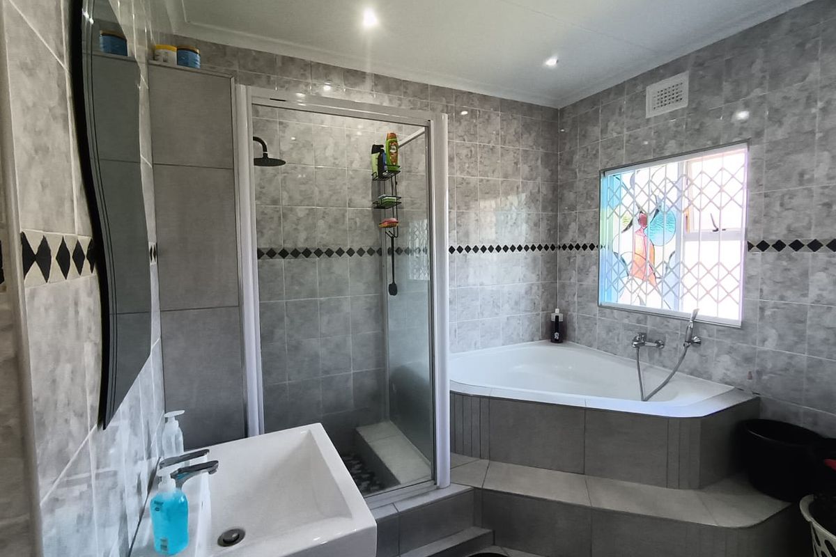 A well-maintained bathroom featuring a corner bathtub, a separate glass-enclosed shower, and a vanity basin with tiled finishes throughout.