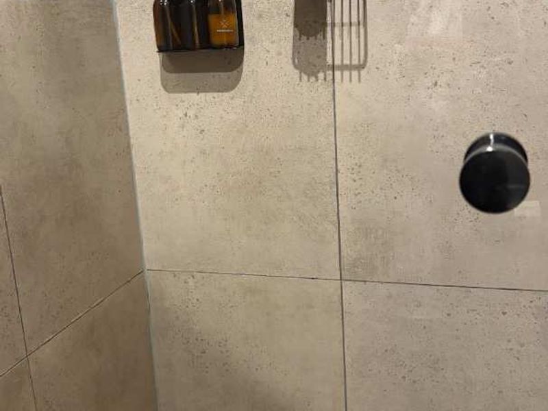 A modern shower enclosure featuring large format neutral wall tiles and a small square tile floor finish with a built-in mixer.
