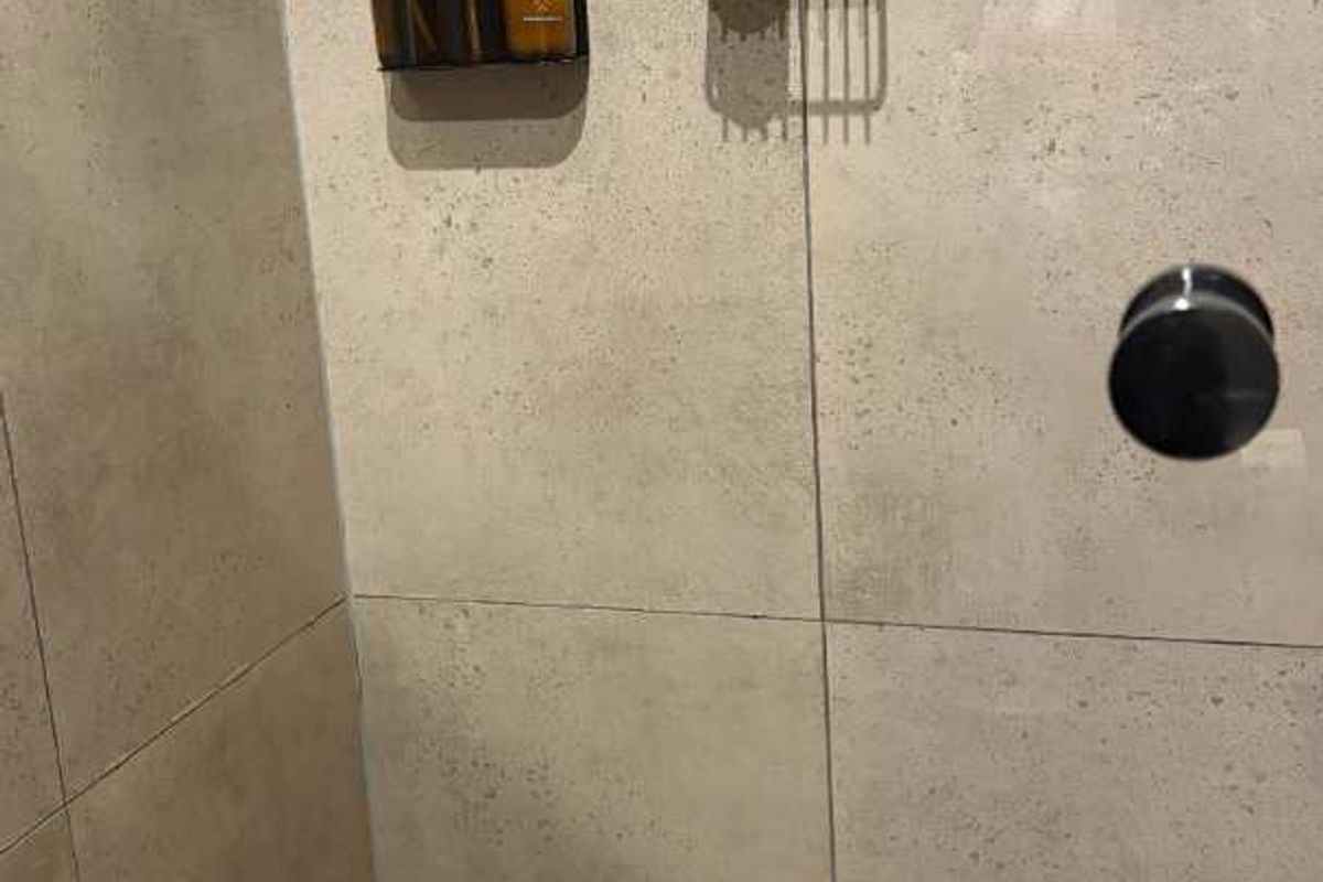 A modern shower enclosure featuring large format neutral wall tiles and a small square tile floor finish with a built-in mixer.