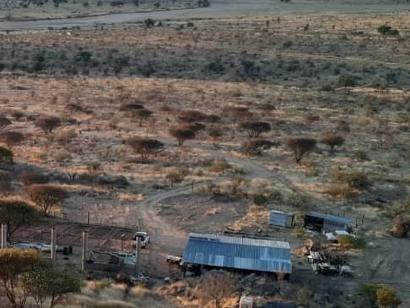 Aerial view of agricultural land featuring a corrugated metal structure, fencing, and expansive natural landscape with distant mountain views.
