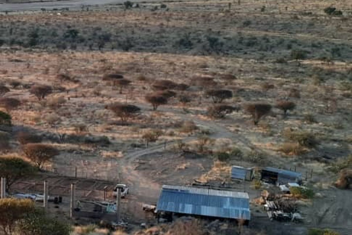 Aerial view of agricultural land featuring a corrugated metal structure, fencing, and expansive natural landscape with distant mountain views.