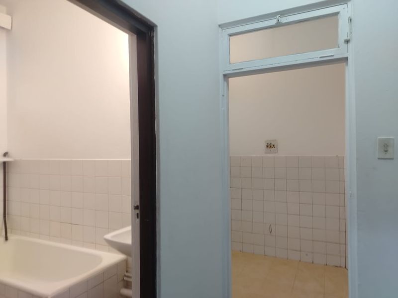A view from a hallway looking into a bathroom and an adjacent utility space, both featuring tiled splashbacks and basic functional fixtures.