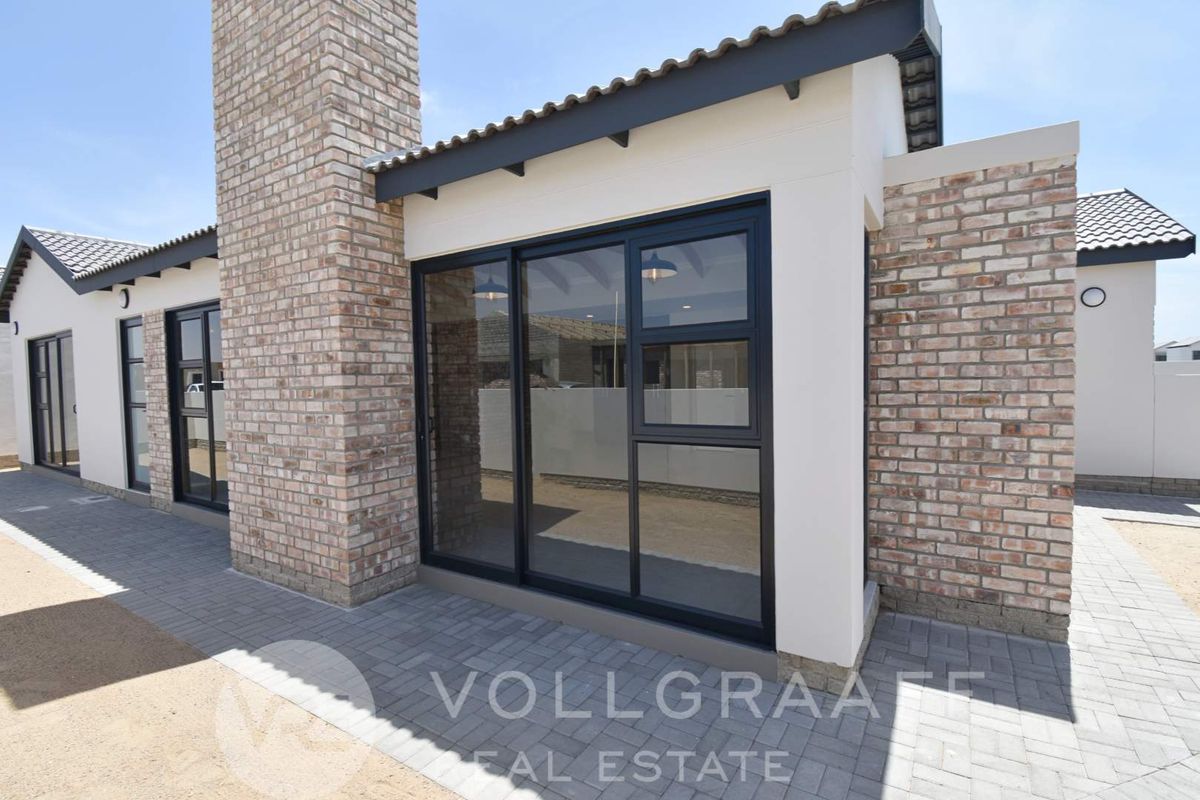 A modern exterior view of the property featuring face brick walls, a prominent brick chimney, and dark-framed sliding glass doors leading to a paved patio.