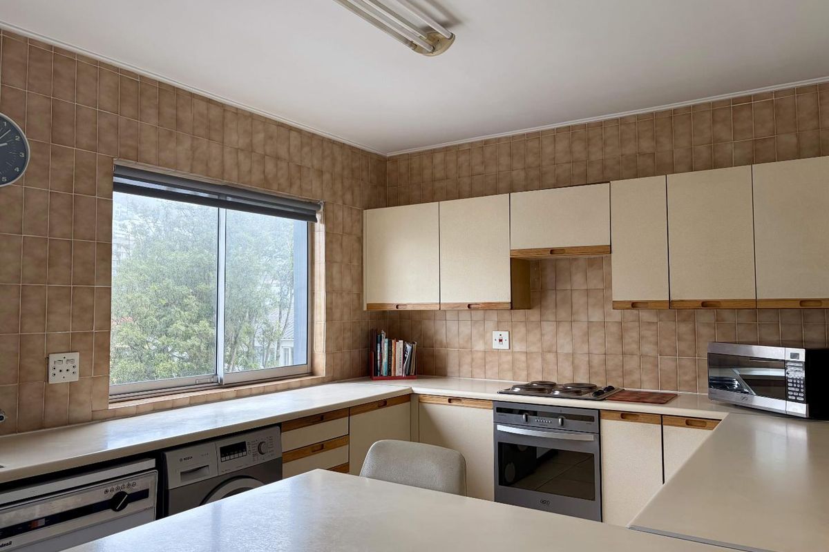 A functional kitchen featuring built-in cabinetry, laminate countertops, a built-in oven, and an electric hob, finished with classic ceramic wall tiling.