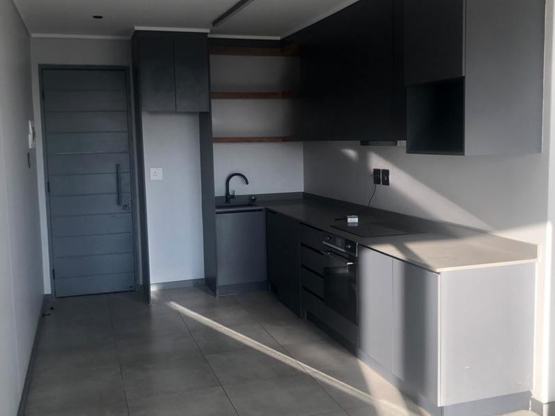 Modern kitchen featuring sleek dark cabinetry, stone countertops, integrated oven, and hob, complemented by neutral tiled flooring and recessed lighting.