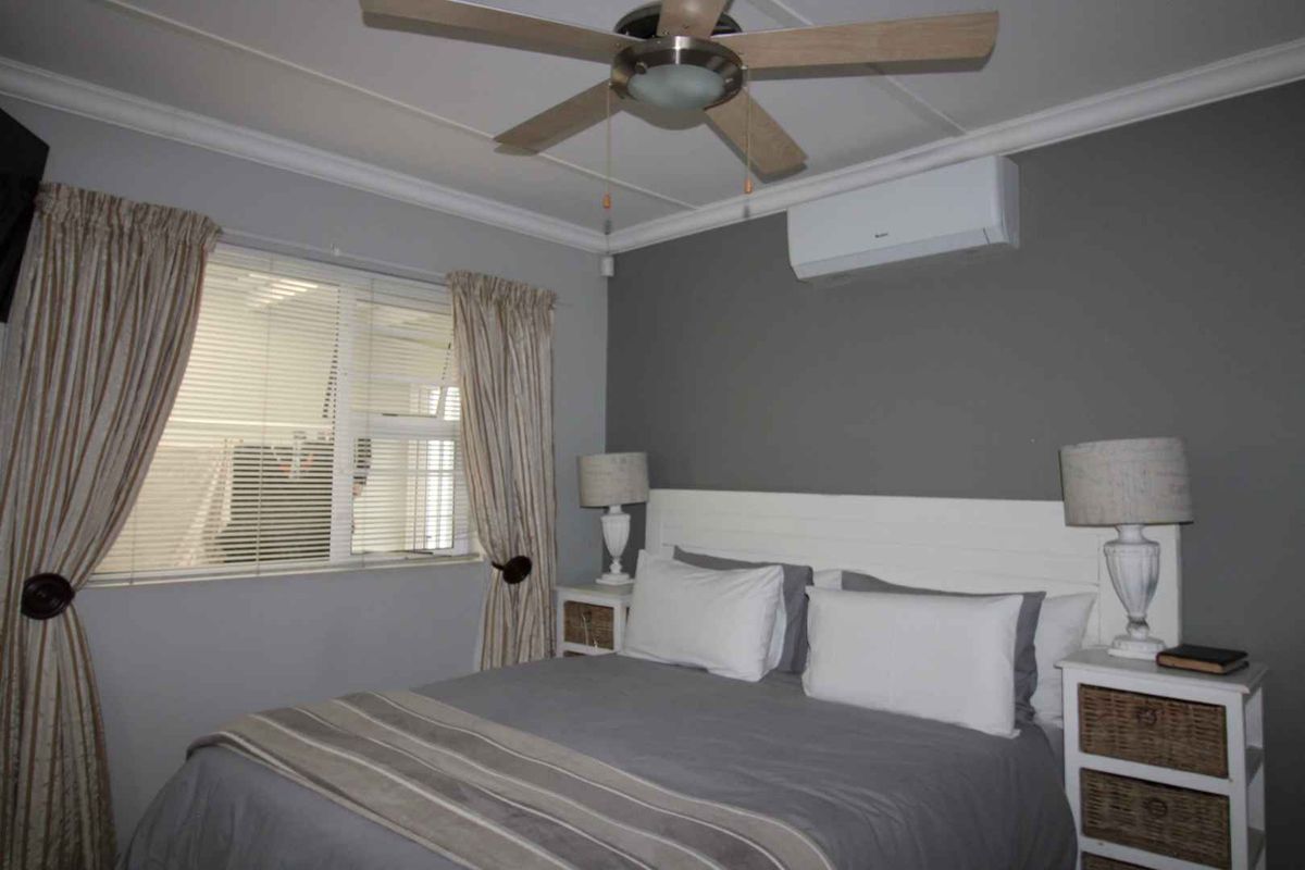 A well-maintained bedroom featuring a ceiling fan, wall-mounted air conditioning unit, and large window with blinds.