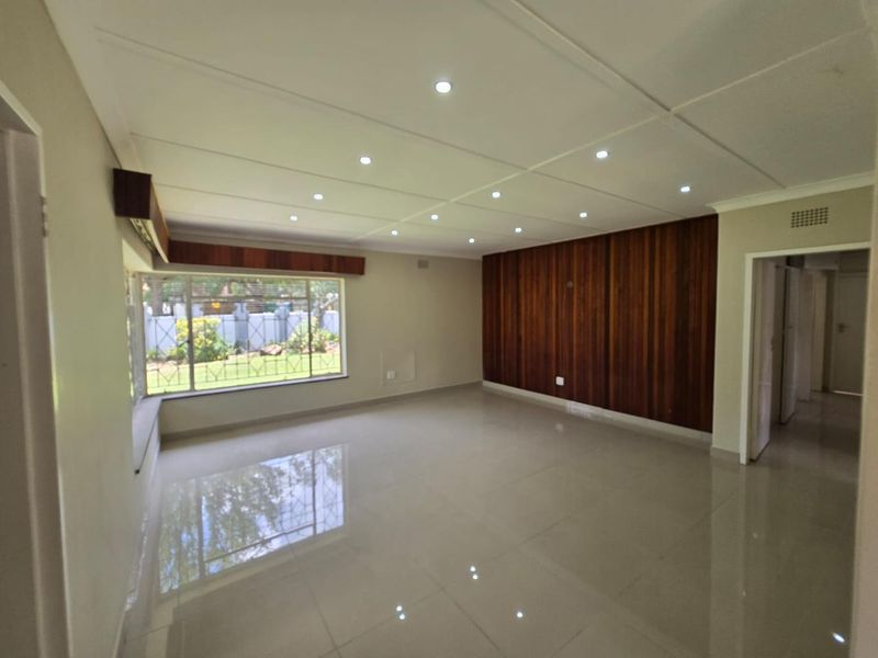 Spacious living area featuring polished tiled floors, recessed ceiling downlights, and a prominent timber-paneled feature wall with large windows overlooking the garden.