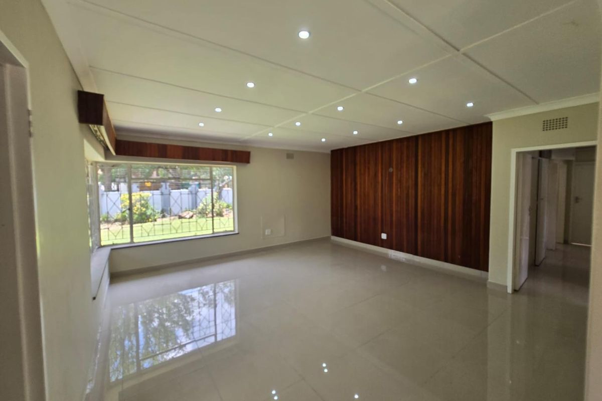 Spacious living area featuring polished tiled floors, recessed ceiling downlights, and a prominent timber-paneled feature wall with large windows overlooking the garden.