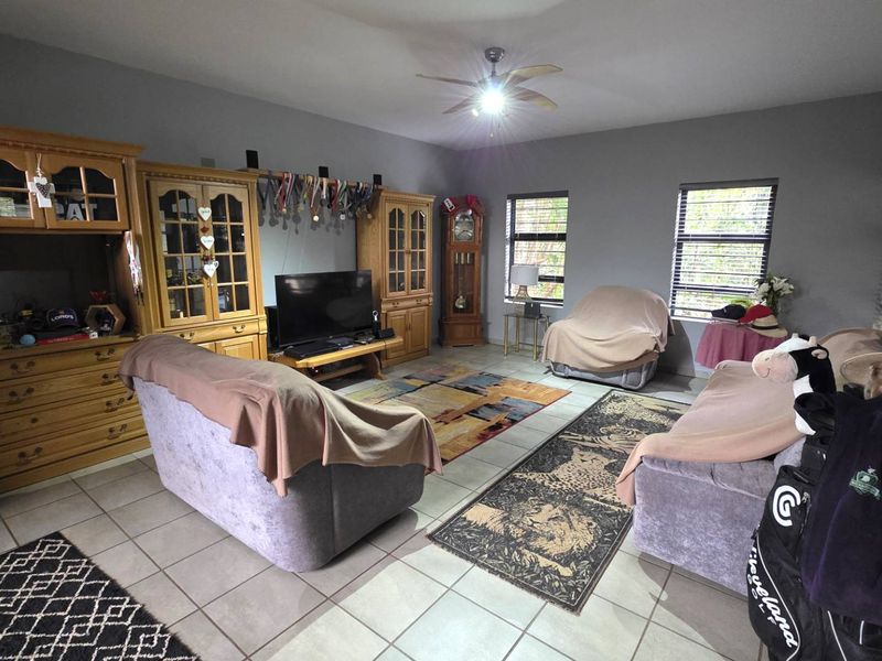Spacious living room featuring neutral tiled flooring, a central ceiling fan, and extensive built-in wooden cabinetry for storage and display.