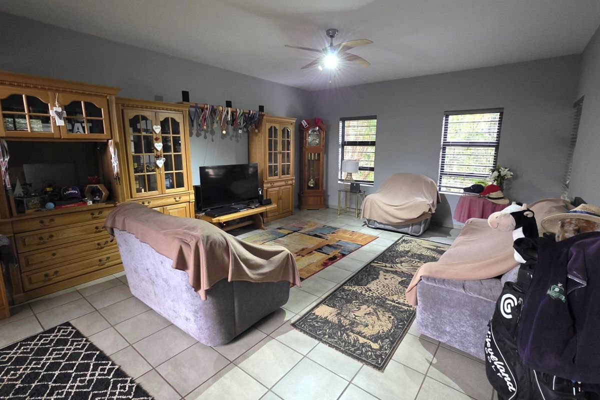 Spacious living room featuring neutral tiled flooring, a central ceiling fan, and extensive built-in wooden cabinetry for storage and display.