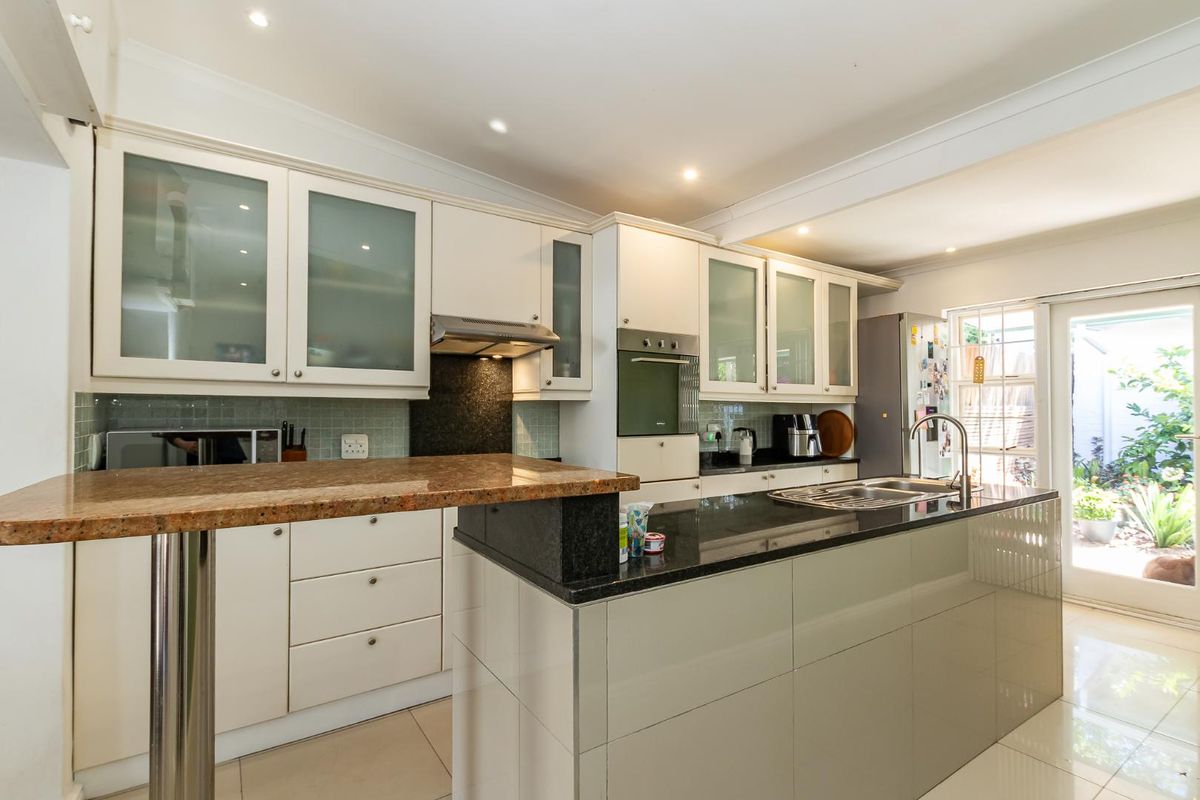 Modern kitchen featuring a central island with granite countertops, built-in oven, extractor fan, and glass-fronted cabinetry, leading out to a private garden area.
