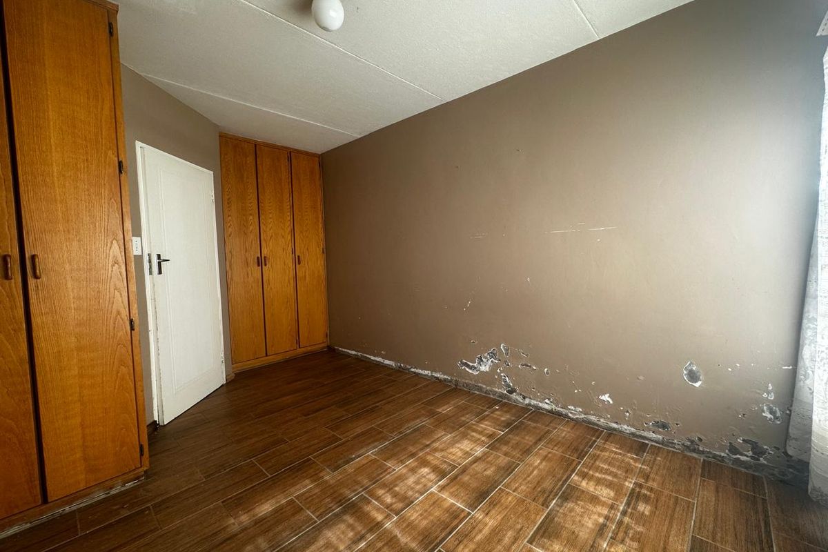 A bedroom featuring wood-look tiled flooring and built-in wooden cabinetry, requiring wall repairs and maintenance.