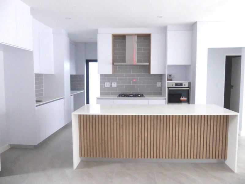 Modern kitchen featuring a central island with slatted wood detailing, white cabinetry, quartz countertops, subway tile backsplash, and integrated stainless steel appliances.