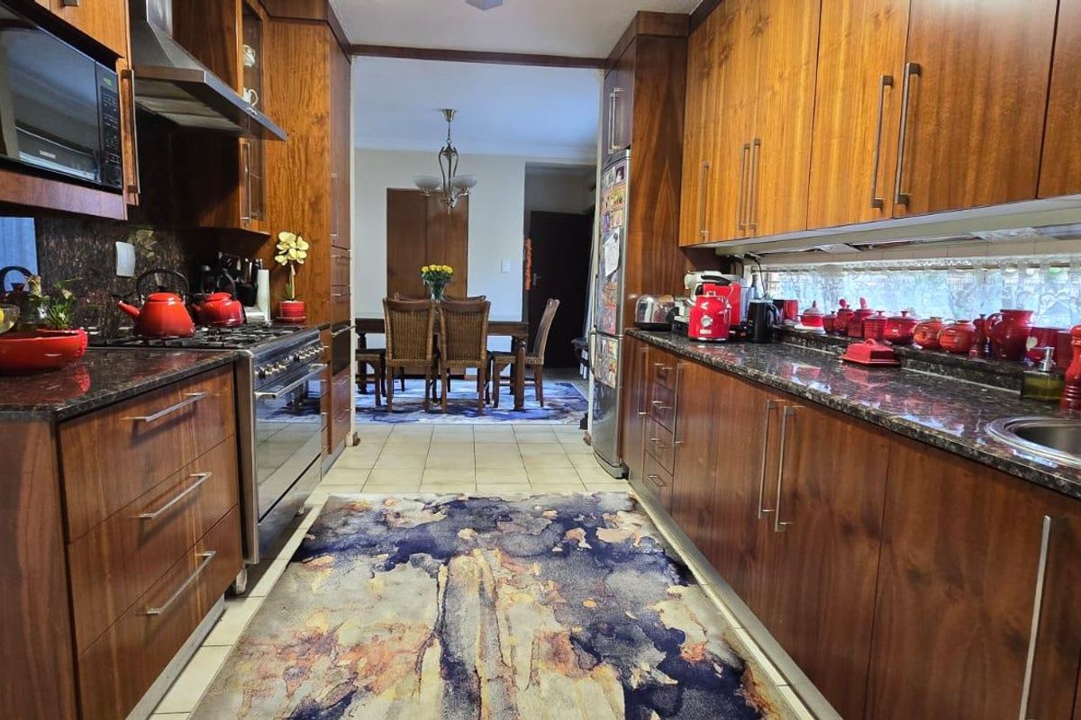 Galley-style kitchen featuring rich wood cabinetry, granite countertops, stainless steel gas range, and integrated extractor fan, leading into an adjacent dining area.