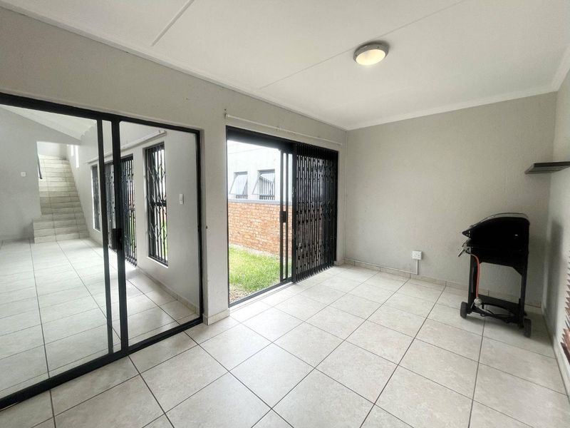 A covered patio area featuring tiled flooring, sliding glass doors with security gates, and direct access to the garden.