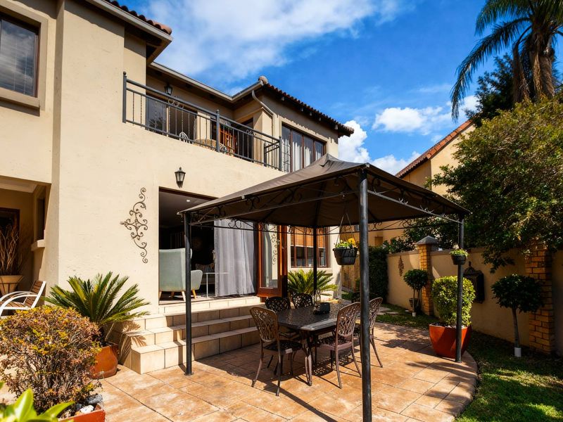 Rear view of the townhouse featuring a tiled patio area, upper-level balcony with wrought iron railing, and a private garden space.