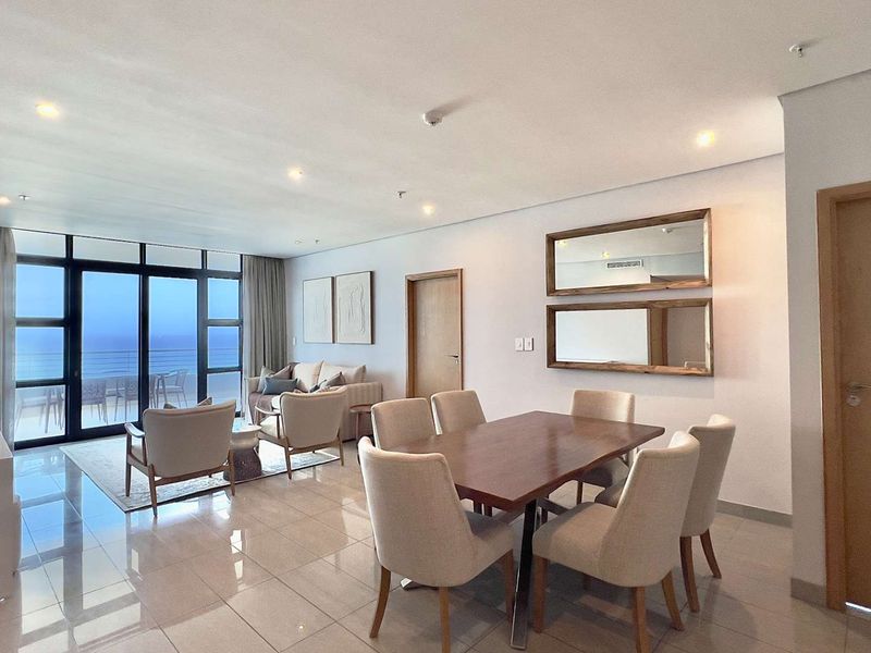 Spacious open-plan living and dining area featuring large sliding glass doors with ocean views, tiled flooring, and modern recessed lighting.