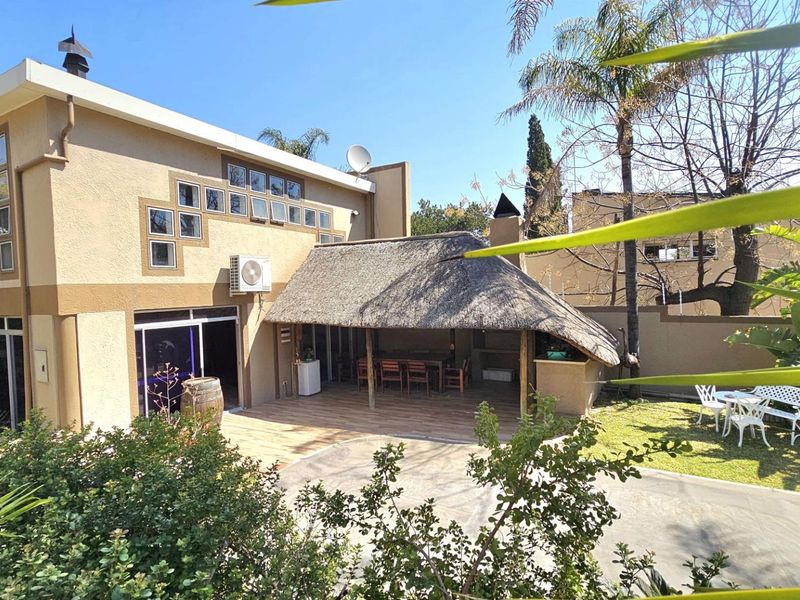 Rear exterior view featuring a spacious tiled patio with a thatched roof lapa, built-in braai area, and well-maintained garden space.