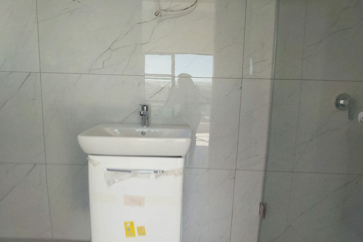 Modern bathroom featuring marble-look wall tiles, a wall-mounted vanity with basin, and a glass shower enclosure in a newly finished space.