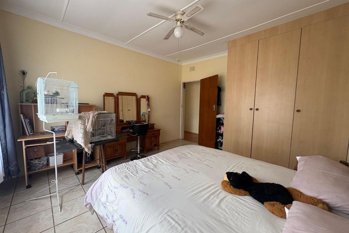 A bedroom featuring built-in wooden cupboards, tiled flooring, and a ceiling fan, offering a functional and practical living space.