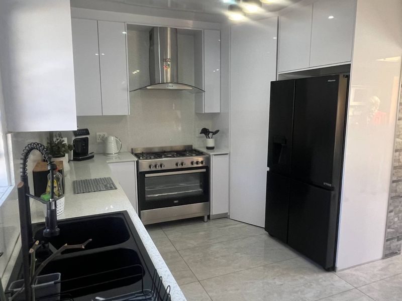 Modern kitchen featuring white high-gloss cabinetry, stone countertops, a gas stove with stainless steel extractor, and sleek tiled flooring.