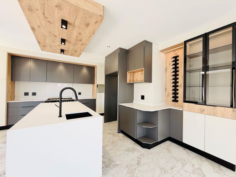 Modern, high-end kitchen featuring a large island with a stone countertop, sleek grey cabinetry, integrated display shelving, and premium marble-look floor tiles.