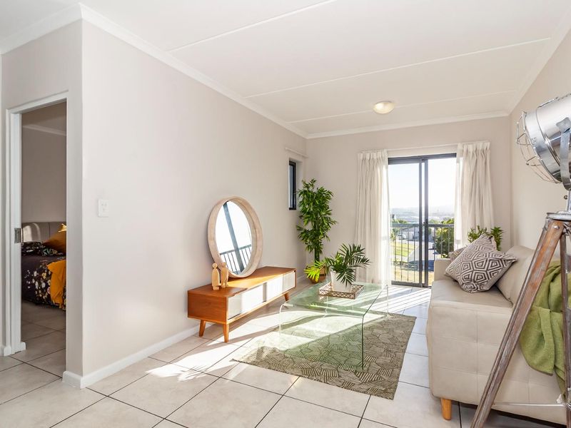 A bright living room featuring neutral tiled flooring and a sliding glass door that provides access to a balcony with natural light.