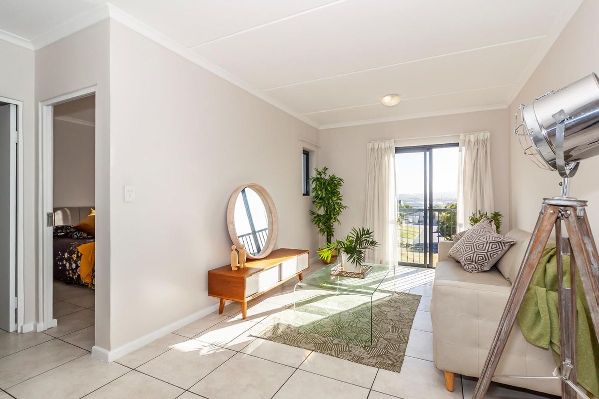 A bright living room featuring neutral tiled flooring and a sliding glass door that provides access to a balcony with natural light.