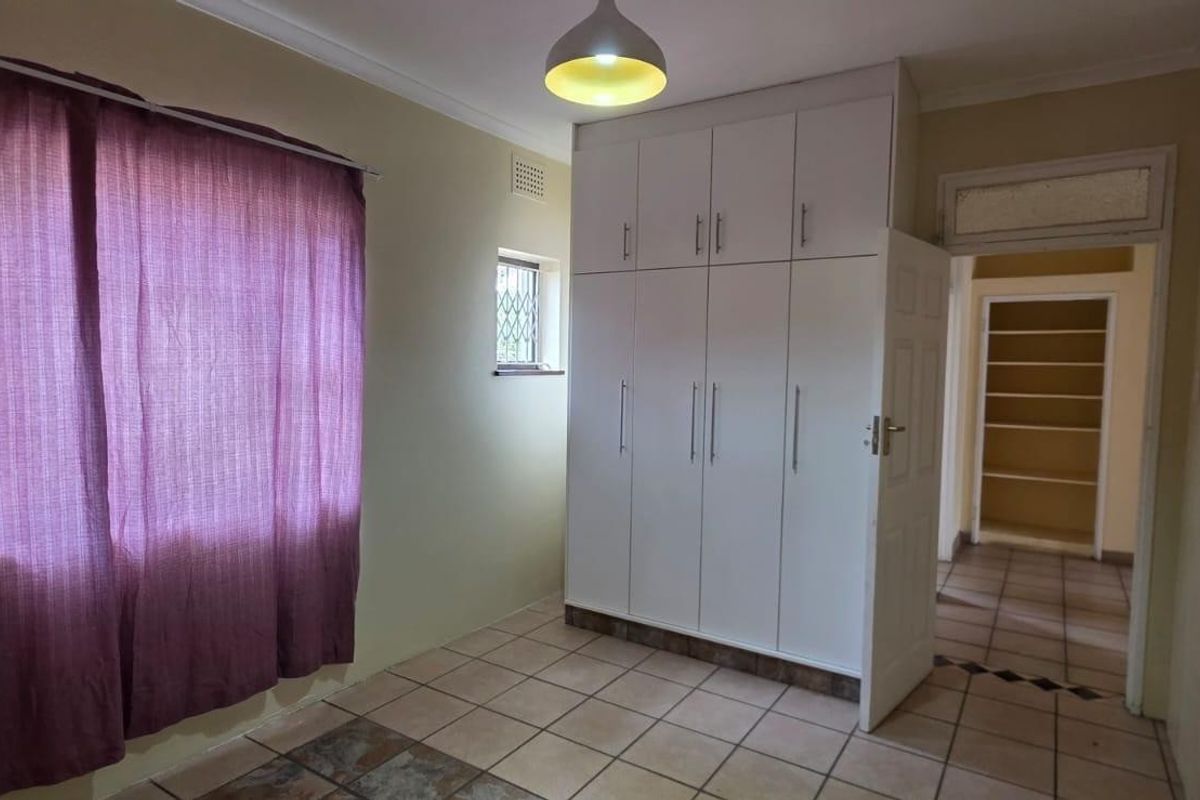 A bedroom featuring tiled flooring, built-in cupboards, and a window with a security gate, offering a clean and functional space.